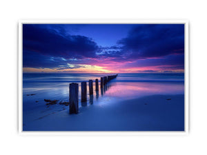Blue sunset beach photography wall art with ocean pier posts for modern living room decor.
