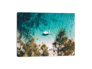Aerial turquoise cove with white boat and pine trees for calming coastal wall art.