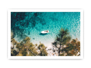 Aerial turquoise cove with white boat and pine trees for calming coastal wall art.