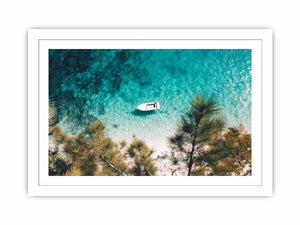 Aerial turquoise cove with white boat and pine trees for calming coastal wall art.