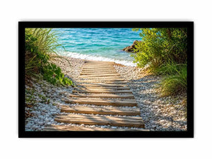 Rustic wooden pathway leading across a pebble beach toward turquoise ocean waves