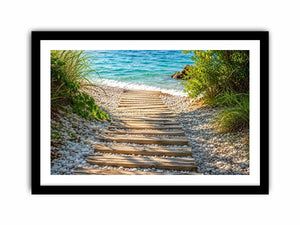 Rustic wooden pathway leading across a pebble beach toward turquoise ocean waves