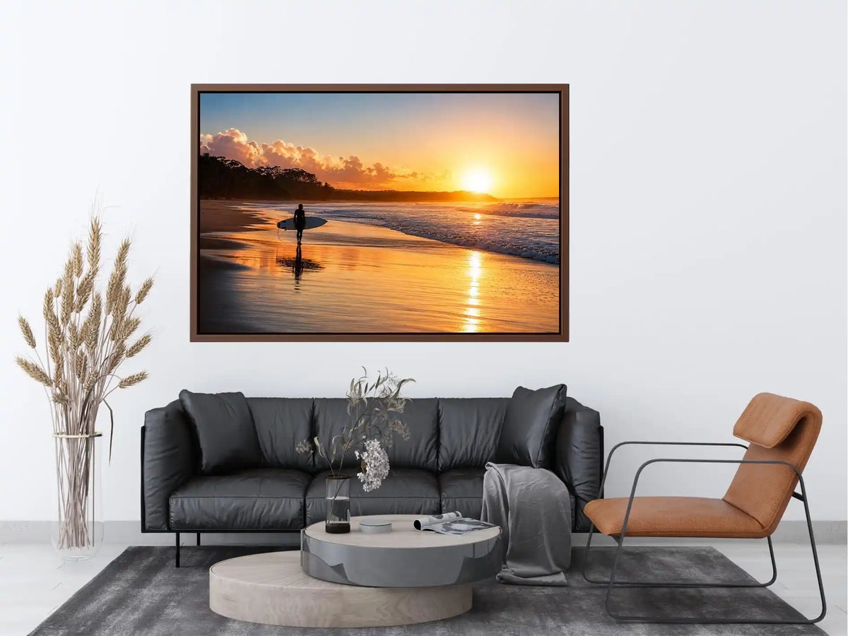 Lone surfer standing on a beach at sunset with golden reflections across calm ocean waves