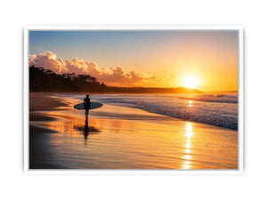 Lone surfer standing on a beach at sunset with golden reflections across calm ocean waves