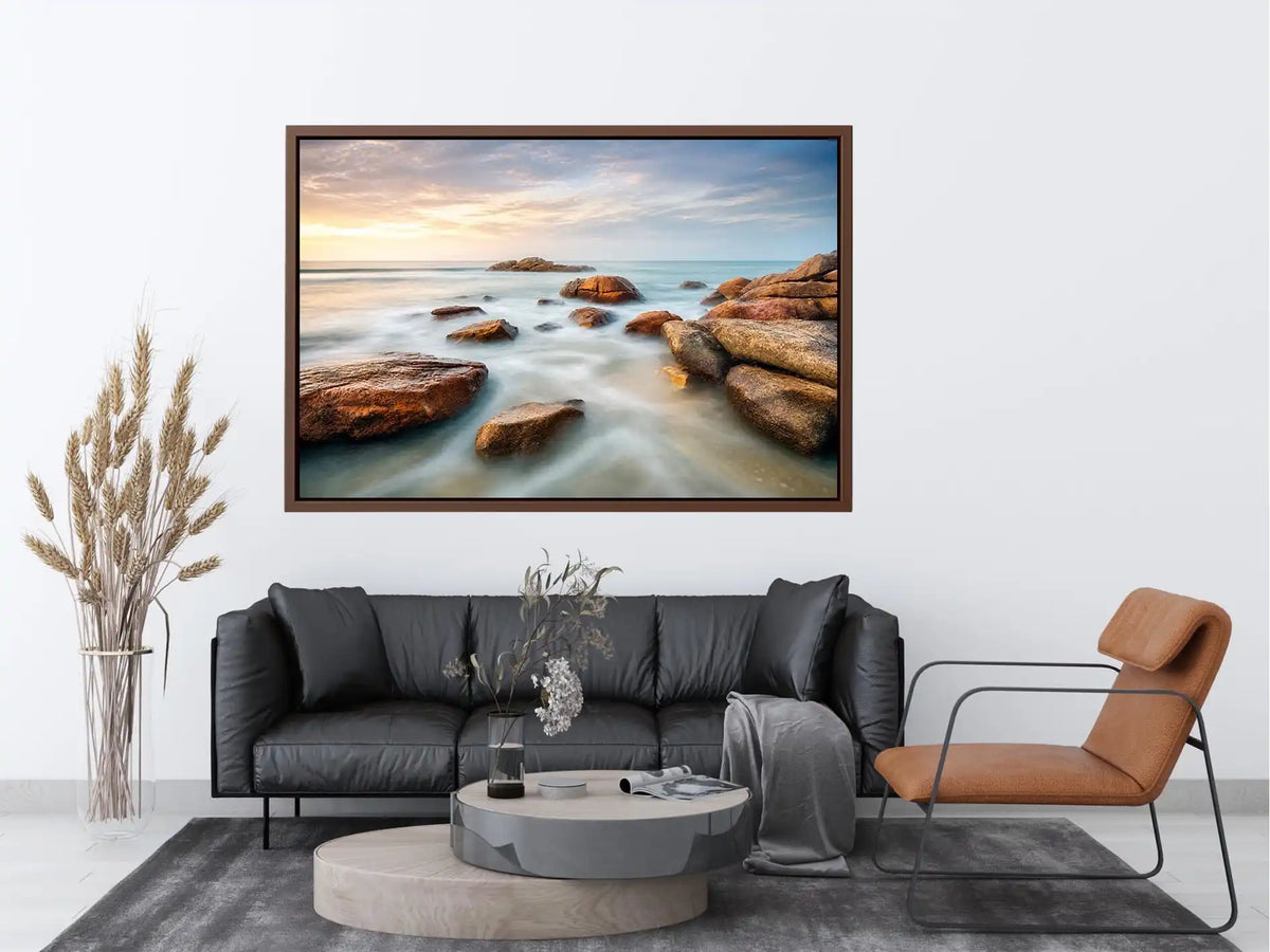 Serene coastal landscape wall art featuring smooth ocean waves, natural shoreline rocks, pastel sunrise sky, and luxury long exposure beach photography for modern coastal interiors