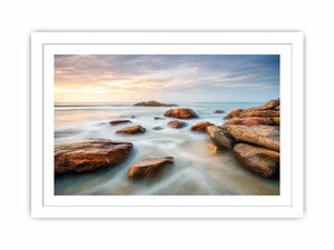 Serene coastal landscape wall art featuring smooth ocean waves, natural shoreline rocks, pastel sunrise sky, and luxury long exposure beach photography for modern coastal interiors