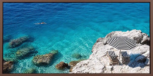 Turquoise coastal cove canvas art with white rocks, striped umbrella and clear sea.