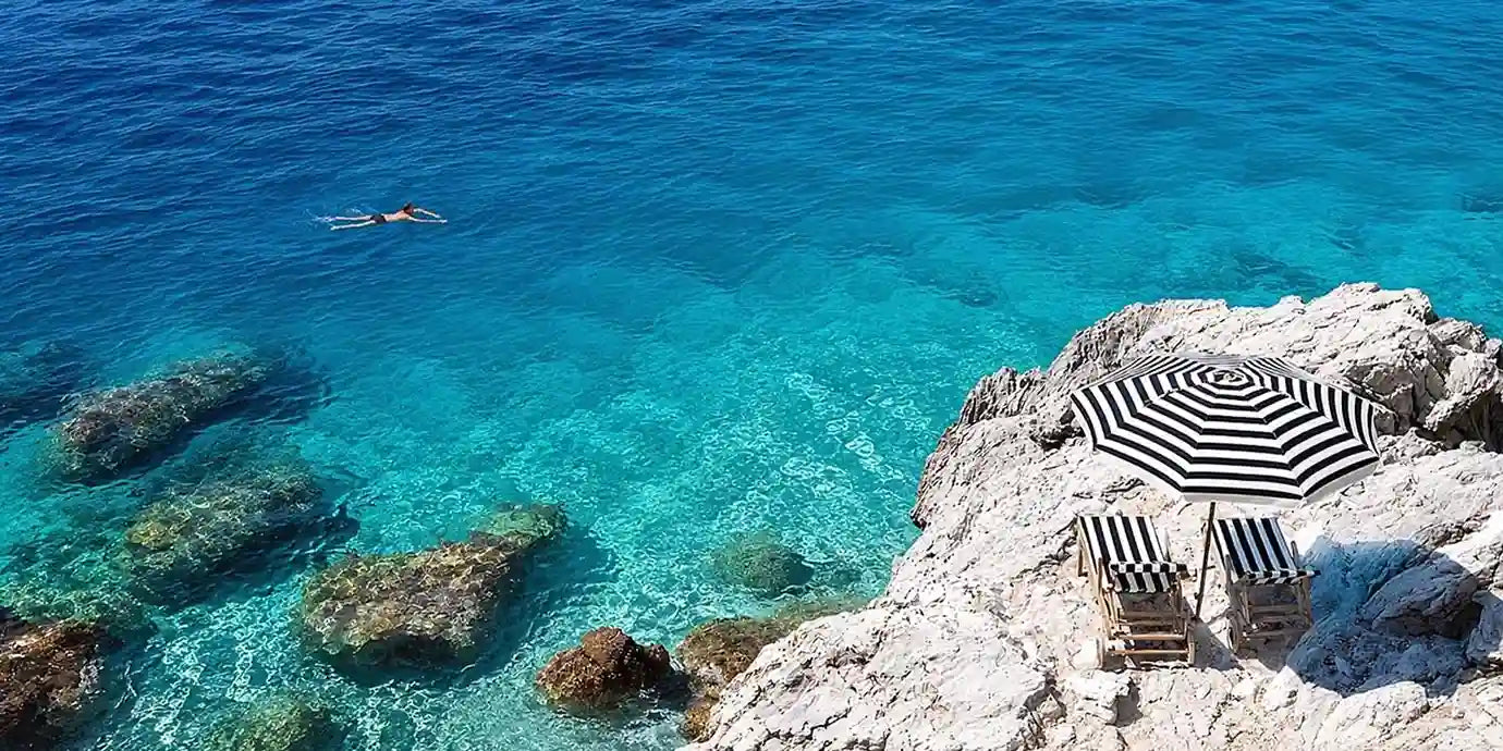 Turquoise coastal cove canvas art with white rocks, striped umbrella and clear sea.