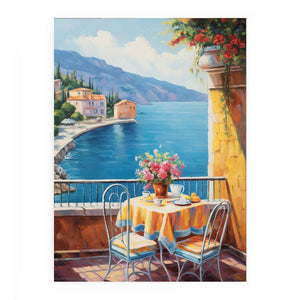 Mediterranean balcony canvas art with blue sea, yellow table, flowers, and coastal village view.