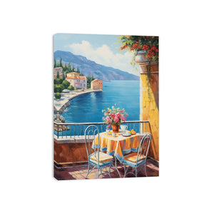 Mediterranean balcony canvas art with blue sea, yellow table, flowers, and coastal village view.