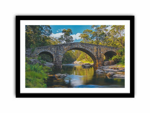 Stone River Crossing a rustic stone bridge spanning a calm river in sunlit woodland