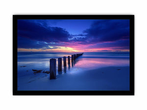 Blue sunset beach photography wall art with ocean pier posts for modern living room decor.