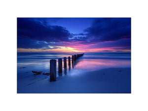 Blue sunset beach photography wall art with ocean pier posts for modern living room decor.