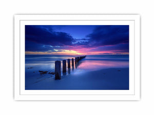 Blue sunset beach photography wall art with ocean pier posts for modern living room decor.