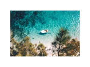 Aerial turquoise cove with white boat and pine trees for calming coastal wall art.