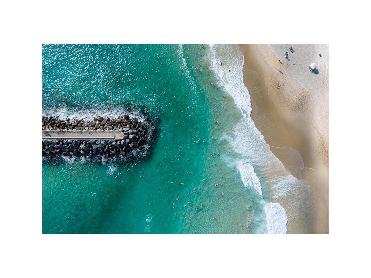 Turquoise beach drone print with swimmers and rock jetty for coastal living room decor