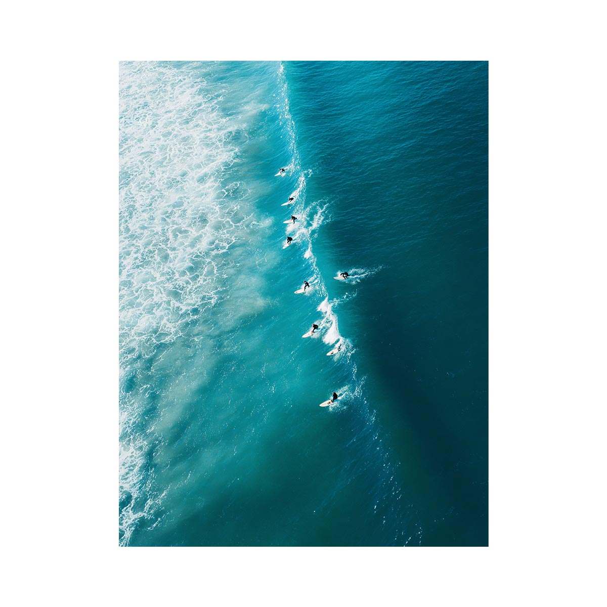 Aerial coastal photography of surfers on turquoise ocean waves for modern beach house decor.