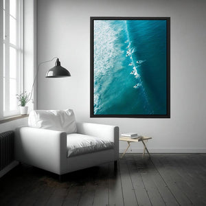 Aerial coastal photography of surfers on turquoise ocean waves for modern beach house decor.