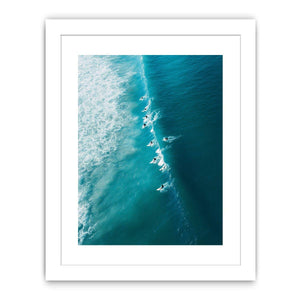 Aerial coastal photography of surfers on turquoise ocean waves for modern beach house decor.