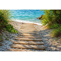 Rustic wooden pathway leading across a pebble beach toward turquoise ocean waves