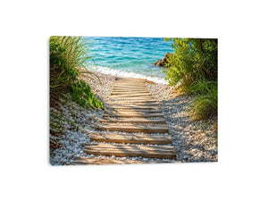 Rustic wooden pathway leading across a pebble beach toward turquoise ocean waves