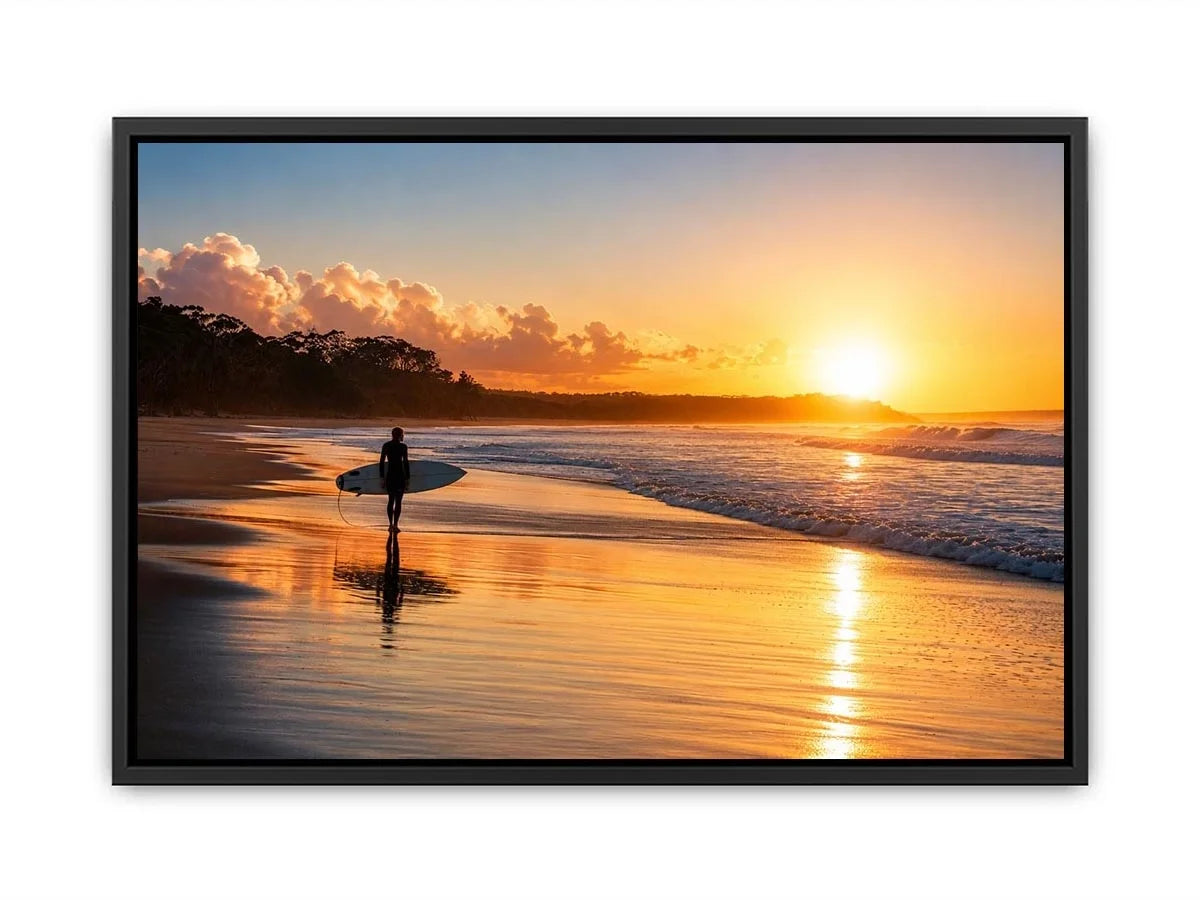 Lone surfer standing on a beach at sunset with golden reflections across calm ocean waves