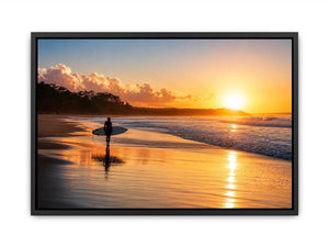 Lone surfer standing on a beach at sunset with golden reflections across calm ocean waves