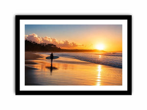 Lone surfer standing on a beach at sunset with golden reflections across calm ocean waves