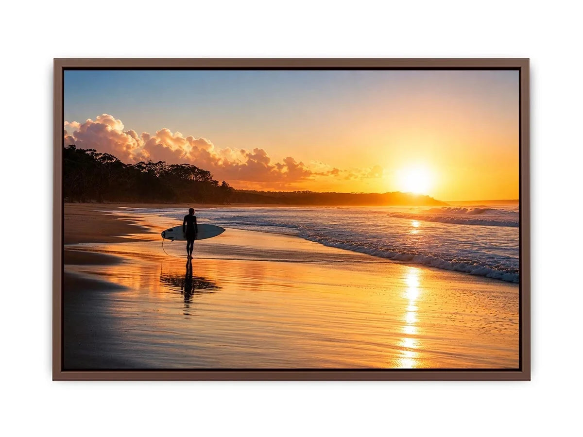 Lone surfer standing on a beach at sunset with golden reflections across calm ocean waves