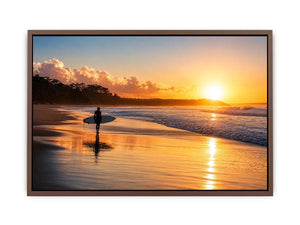 Lone surfer standing on a beach at sunset with golden reflections across calm ocean waves