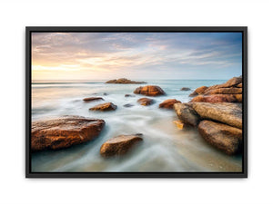 Serene coastal landscape wall art featuring smooth ocean waves, natural shoreline rocks, pastel sunrise sky, and luxury long exposure beach photography for modern coastal interiors