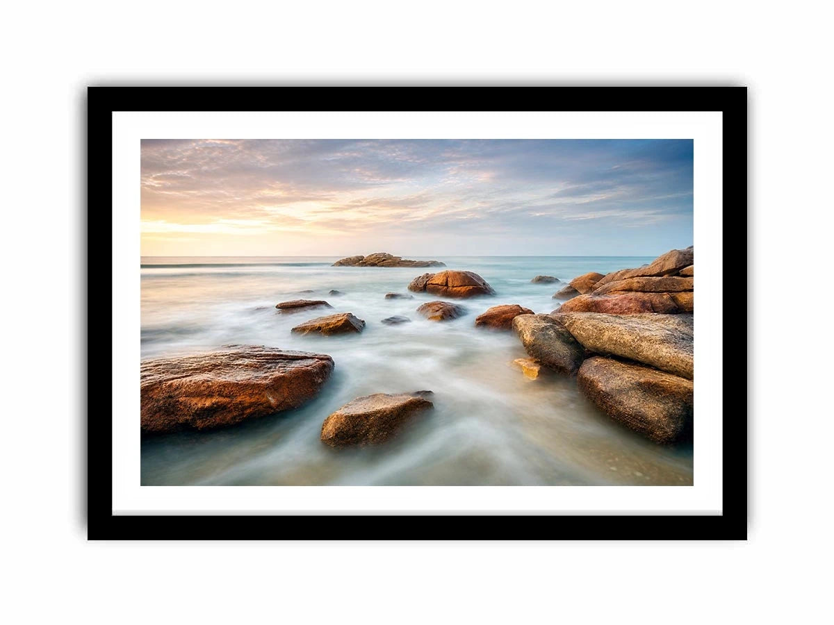 Serene coastal landscape wall art featuring smooth ocean waves, natural shoreline rocks, pastel sunrise sky, and luxury long exposure beach photography for modern coastal interiors