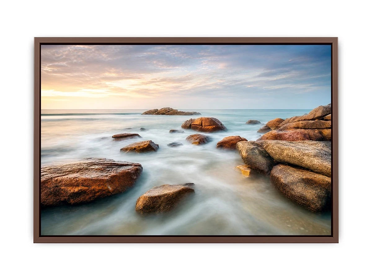 Serene coastal landscape wall art featuring smooth ocean waves, natural shoreline rocks, pastel sunrise sky, and luxury long exposure beach photography for modern coastal interiors