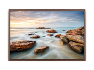 Serene coastal landscape wall art featuring smooth ocean waves, natural shoreline rocks, pastel sunrise sky, and luxury long exposure beach photography for modern coastal interiors