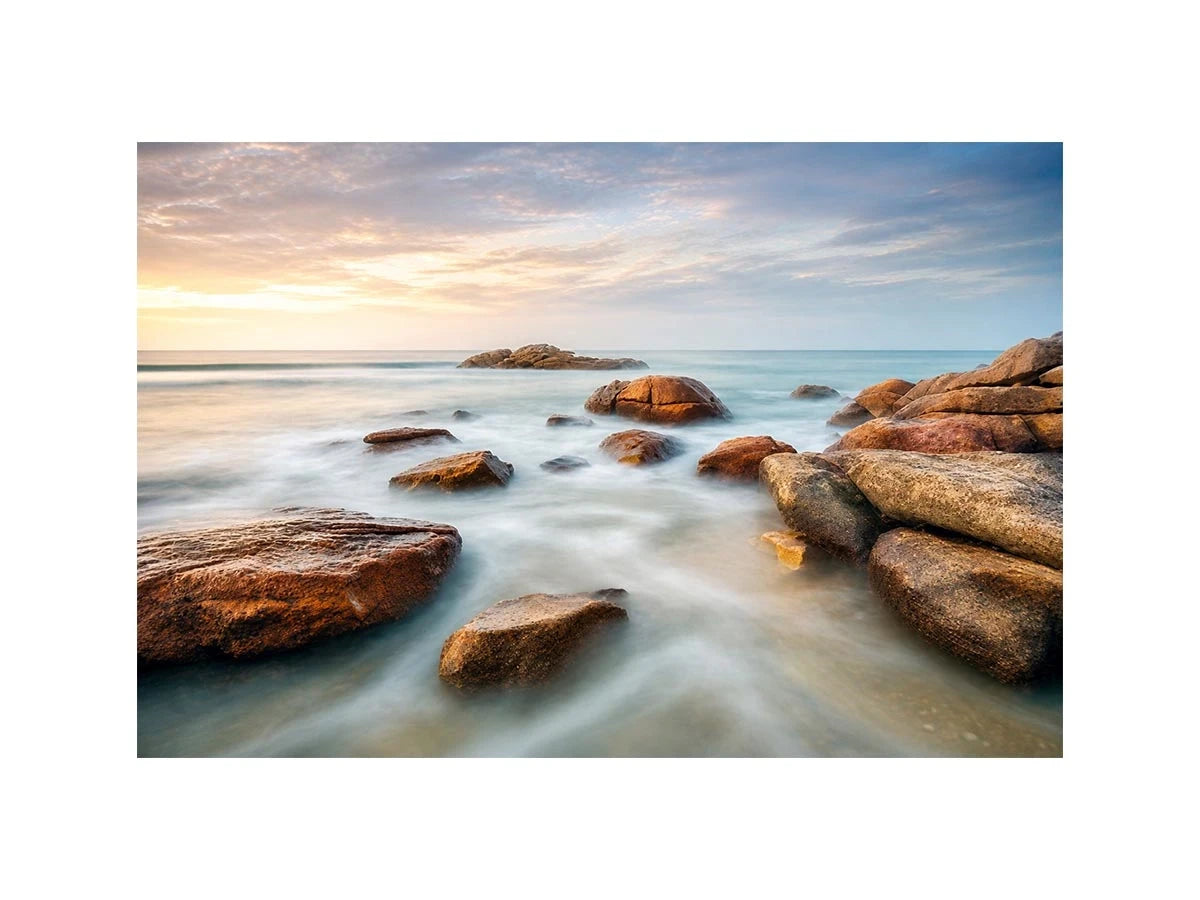 Serene coastal landscape wall art featuring smooth ocean waves, natural shoreline rocks, pastel sunrise sky, and luxury long exposure beach photography for modern coastal interiors