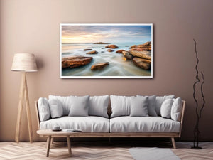 Serene coastal landscape wall art featuring smooth ocean waves, natural shoreline rocks, pastel sunrise sky, and luxury long exposure beach photography for modern coastal interiors