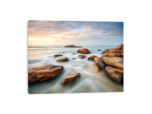 Serene coastal landscape wall art featuring smooth ocean waves, natural shoreline rocks, pastel sunrise sky, and luxury long exposure beach photography for modern coastal interiors