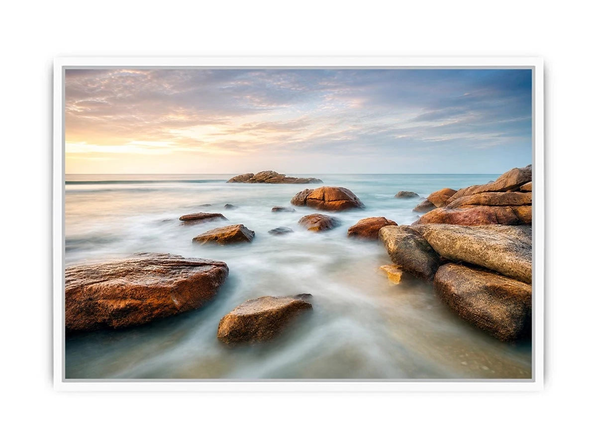 Serene coastal landscape wall art featuring smooth ocean waves, natural shoreline rocks, pastel sunrise sky, and luxury long exposure beach photography for modern coastal interiors