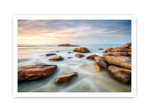 Serene coastal landscape wall art featuring smooth ocean waves, natural shoreline rocks, pastel sunrise sky, and luxury long exposure beach photography for modern coastal interiors