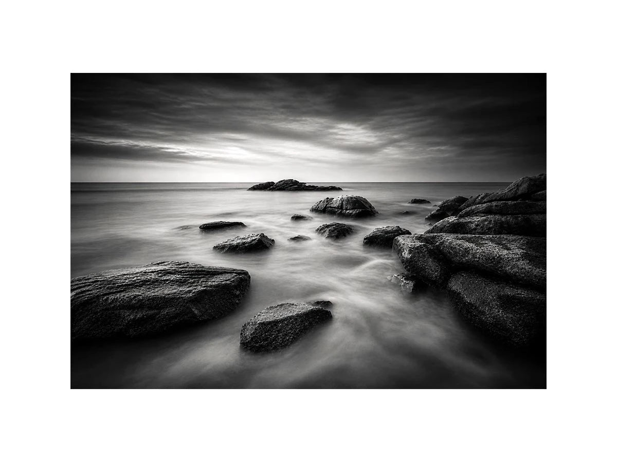 Black and white ocean wall art with dramatic coastal rocks, misty waves, and moody storm clouds in contemporary monochrome seascape style