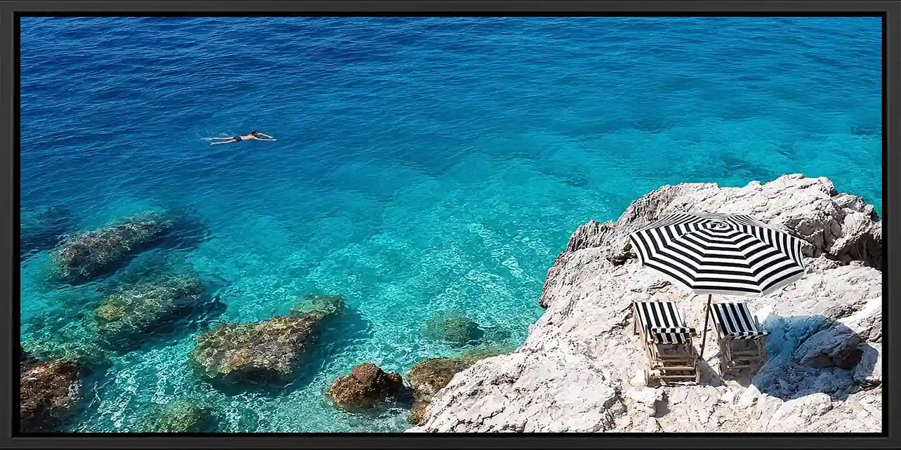 Turquoise coastal cove canvas art with white rocks, striped umbrella and clear sea.