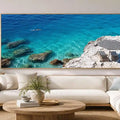 Turquoise coastal cove canvas art with white rocks, striped umbrella and clear sea.